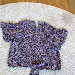 Leopardmönstrad blus med knytning. Lila, Lindex - Säljer en lila leopardmönstrad blus. I typ silkesmaterial och med knapp i nacken. Lindex-134/140