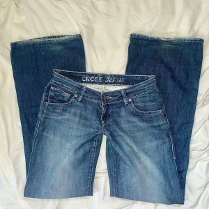 Blå jeans från Cross Jeans - Säljer ett par vintage blå jeans från Cross Jeans med stora backfickor. de har vida ben och är utsvängda och sitter lågmidjade. strl W28 = S och längden är 32 och innerbenslängden är ungefär 82cm
