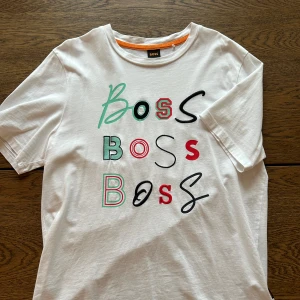 Hugo boss t-shirt vit - En vit t-shirt från Hugo boss med motiv i olika färger. Väldigt sparsamt använd. Storlek S men sitter som en medium. 