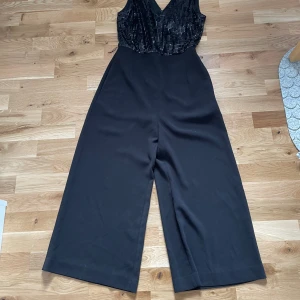 Festlig jumpsuit  - Svart festlig jumpsuit med paljetter från H&M säljes. Använd ett fåtal gånger och i gott skick. Tillhör även ett tygskärp som inte finns med på bilden. Säljes för 50 kr. 