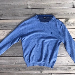 Ljusblå stickad Ralph Lauren tröja - Jag säljer en stickad tröja av märket Ralph Lauren eftersom den inte används längre. Skicket är 10/10 utan några defekter alls. Färgen syns bättre på bild 1 & 3 pga ljuset. Köpt för 1600 kr på NK Sthlm. Storleken är M och  passar folk runt 180cm.