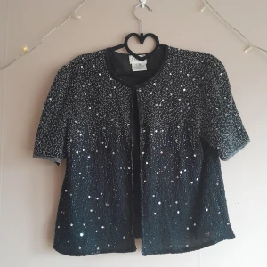 Glittrig bolero/kortärmad kofta - Superfin kortärmad bolero med glitter & paljetter. Köpt vintage. Knäppning med hyskor hela vägen. Storleken uppskattas till M-L.  Katt finns i hemmet. Önskar du fler bilder? Skriv till mig! 🌼