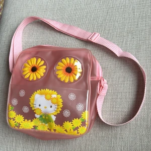 Väska Hello Kitty - Söt väska i rosa genomskinligt plast-material. Genomskinligt fack med Hello Kitty på framsidan. Stort fack med dragkedja. Justerbar axelrem. Storlek ca 22x22 cm