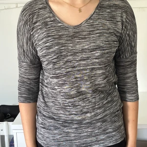 Gråmelerad tröja från Vero Moda - En bekväm gråmelerad tröja från Vero Moda med trekvartsärm och rund halsringning. Tröjan har en normal passform och är tillverkad i ett mjukt material.