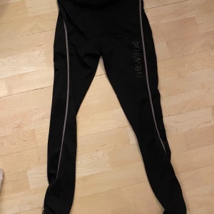 Svarta träningsleggings från Newline - Säljer ett par svarta träningsleggings från Newline i storlek S. De är tighta och har en snygg design med gråa detaljer längs benen. Perfekta för träning och löpning. De är i bra skick och redo för nya äventyr!