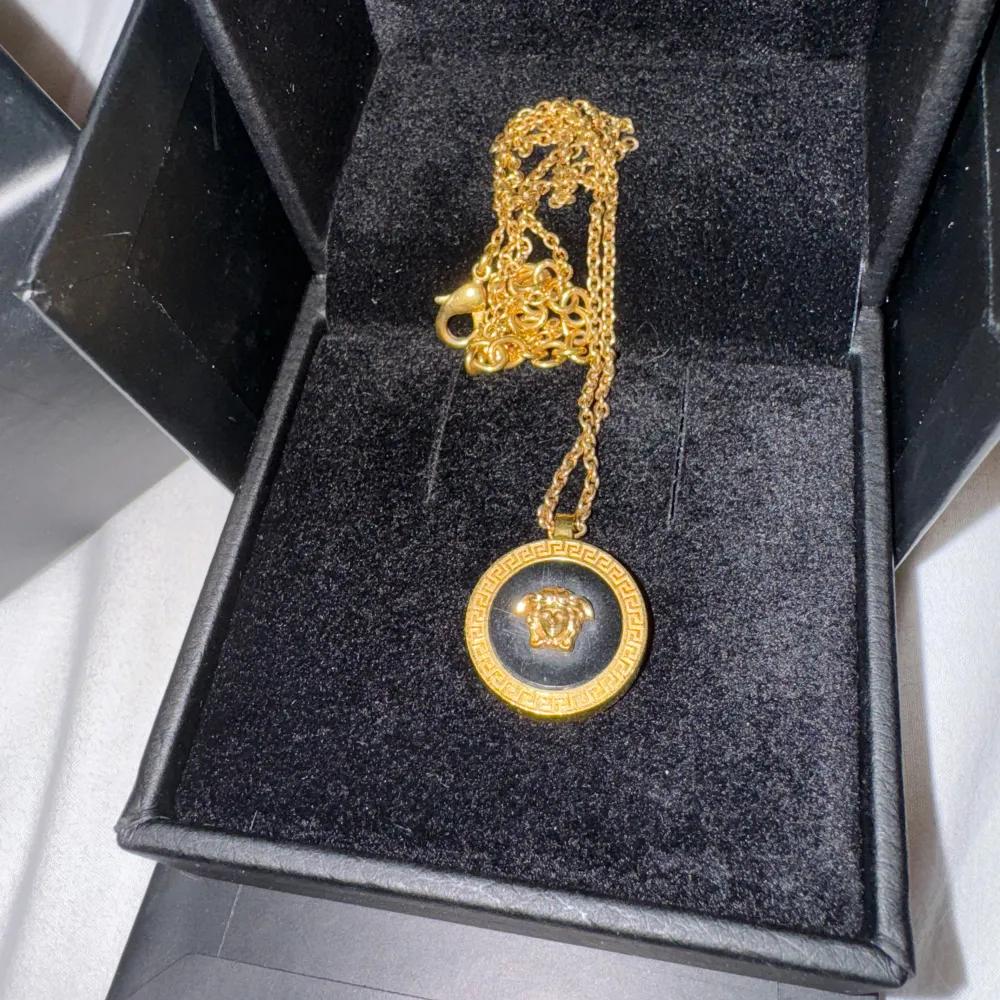 Säljer ett snyggt guldhalsband från Versace. Halsbandet har en rund medaljong med Versaces ikoniska Medusa-huvud i mitten och en grekisk nyckel-design runt kanten. Perfekt för att ge din outfit en lyxig touch!. Accessoarer.