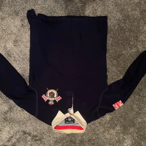 Mörkblå tröja från La Martina - Säljer en snygg mörkblå tröja från La Martina i storlek S. Tröjan har långa ärmar och en broderad logga på bröstet. Den har en krage med en kontrasterande färg på insidan. Perfekt för höst och vinter!