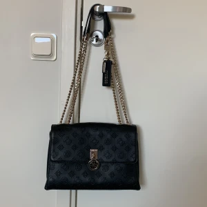 Snygg Guess axelremsväska - Fin äkta väska från Guess . Finns tecken på användning, men lädret i fint skick. Kedjan har blivit missfärgad på en del ställen, men ingenting man tänker på. Köpt för 1500kr, hör av dig vid frågor💗