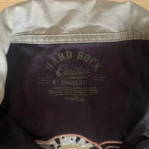 Grå och svart kortärmad skjorta från Hard Rock Guitar Company - Säljer en cool grå och svart kortärmad skjorta från Hard Rock Guitar Company. Skjortan har knappar hela vägen fram och två bröstfickor med lock. Perfekt för en avslappnad stil eller för att rocka på en fest! 🎸