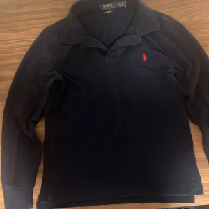 Ralph Lauren Pike - Säljer en snygg mörk blå långärmad pikétröja från Polo Ralph Lauren. Storleken S och tröjan har inga hål eller skador. Tröjan är i slim fit och har en klassisk krage med knappar. Den har också den snygga röda Polo Ralph Lauren-loggan broderad på bröstet. Perfekt för hösten