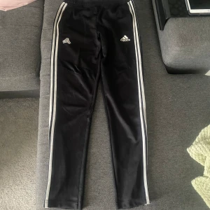 Svarta adidas byxor - Säljer ett par svarta Adidas byxor🤩De har snöre i midjan, så kan passa flera storlekar, fickor med dragkedjor & en slits längst ner med dragkedja på båda sidorna🙌🏻Strl. UK 15-16Y/US XL. I använt skick men bra (lite nopprig & missfärgad på det vita)😊