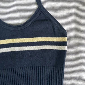 Stickad halterneck croptop - Vintage stickad halterneck topp med öppen rygg, i fint skick. Mörkblå med en pastellgul och en vit linje. Sitter bekvämt och bandet runt nacken går att justera efter eget behov. Skriv gärna till mig om du har fler frågor!<3