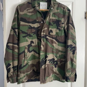 Justjunkies overshkirt - Just Junkies overshirt med camo mönster. Detaljerat med ett stort påsytt badge i tigerform. Stängs med dold blixtlås. Kommer med två sidfickor och en bröstficka Använd men i bra skick! Storlek S, passar liten M Nypris 1.200kr Mitt pris 400kr