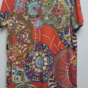 Färgglad mönstrad klänning - En färgglad klänning med ett komplext mönster i olika färger som röd, grön, blå, gul och vit. Klänningen har korta ärmar och ett unikt, detaljerat mönster som täcker hela plagget.