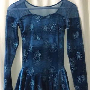 Blå klänning från Mondor - En elegant blå klänning från Mondor med långa ärmar och ett glittrigt blommönster. Klänningen har en transparent övre del och en volangdetalj vid midjan.