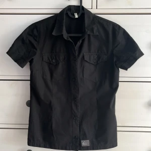 Svart figursydd skjorta  - En supersnygg svart figursydd skjorta med fräck detalj nertill, Okänt märke, strolek S. Köparen står för frakt, finns katt i hemmet!