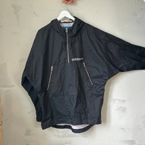 Adidas poncho / regnjacka - Svart Adidasjacka i ponchostuk. Vindjacka/regnjacka. I jättebra skick. Dragkedjor längs med båda sidor för att göra den större. Köparen står för frakten, annars finns den i södra sthlm 😊 Kolla gärna mina andra annonser!