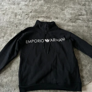 Svart hoodie  - En svart polo hoddie utan luva med ull på insidan från Emporio Armani. Text (märket) på framsidan av tröjan. 