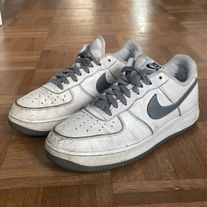 Air force 1 - Air force 1 i storlek 41 Skorna är självdesignade och är vita med grå sula, snöre och logga. Skorna är använda och har en skada i högra hälen. (Se bild)