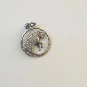 Berlock Väduren  - Liten berlock föreställande stjärntecknet väduren  Okänd metall 