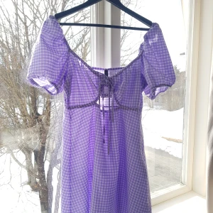 Klänning  - En snygg vardags-klänning som aldig är använd med prislapp kvar! Har en knytbar öppning vid bysten som är så fin Är en ljus lila rutig kläning som går just över knäna💗