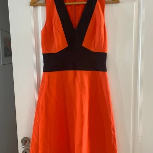 Klänning Hugo Boss stl 34 - Orange och svart sommarklänning från Hugo Boss. Klänningen är i en mycket kroppssmickrande modell. Material i linne, viskose och bomull. 