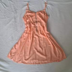 Aprikosfärgad/rosa klänning med blixtlåsdetalj framtill och justerbara axelband.  Använd enstaka gång.