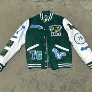 Teddy Varsity jacka - Mörkgrön, vit varsity jacka från American College. Stängs framtill med dragkedja och tryckknappar. Jackans framsida och baksida är tillverkade i ull, ärmar i läder. Patch med textil logotyp. Aldrig använt.  Köptes från johnells 3499 