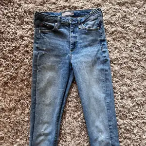 Ett par ljusblåa stretchiga jeans i modellen High Waist Haley, Ankle från Cubus. De har en ”raw hem” och små slitna detaljer. Mått: Midja: 32 cm, beninnerlängd: 70 cm & utsida ben: 93 cm. Plagget är i tippenskick! Storlek S 💙