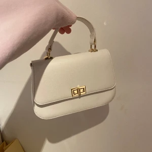 Vit handväska  - Vit liten handväska med gulddetaljer som är oanvänd. Köpt på en butik i Italien därav inget specifikt märke