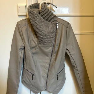 Grå skinnjacka - Helt ny skinnjacka som tråkigt nog aldrig kommit till användning. Kragen kan vikas ner på olika sätt! Skulle säga att den passar XS-S. Köpt för 559 kr. SKINNIMITATION! Läs bio innan köp☺️