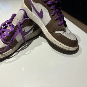 Jordan 1 low - Det är ett par air jordan 1 low de är i gott skick, de är brän Märke som man inte tänker på när man har på sig de. Märket är på den högra skon. De är använda många gånger. De kan behöva bytta snören på de för de är också ganska slitna. Fg brun, lila