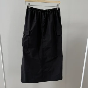 Svart cargokjol - Svart kjol i cargostil från Pull & Bear. Använd två gånger. Dragsko i midjan, liten slits där bak och fickor på sidorna.