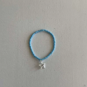 Egengjort pärlarmband  - Ett egengjort pärlarmband med färgeren blå. Armbandet har en berlock i silver som avbildar en stjärna. 