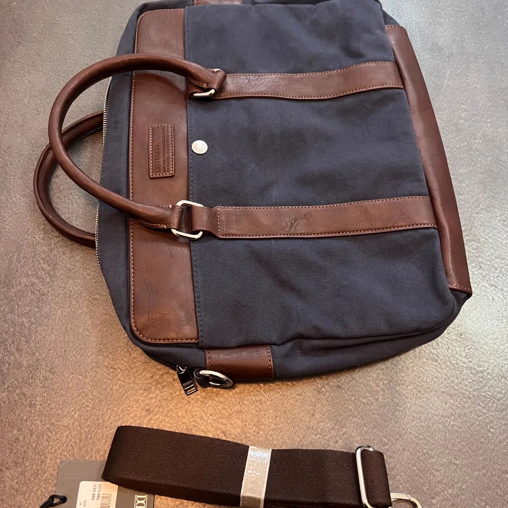 Klassisk laptop väska i marinblått tyg samt mörkbrunt läder. Axelband och lappar finns kvar. Nypris för denna är 699 kronor.. Väskor.