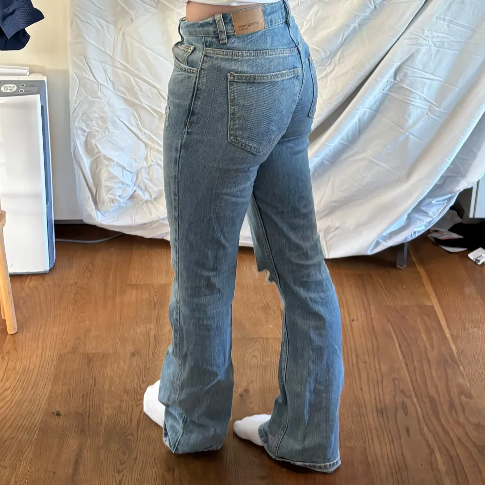Blå jeansbyxor med en rippad detalj på ena knät. Byxorna har en medel hög midja och en bootcut-stil.. Farkut & Housut.