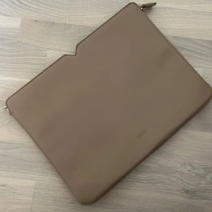 Datorfodral beige  - Datorfodral i beige köpt på Åhléns, använd 1 gång så i fint skick. Finns stort fack inuti. 
