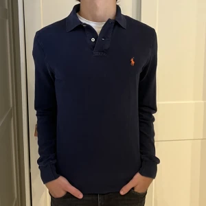 Långärmad Ralph Lauren piké - Långärmad Ralph Lauren piké i färgen mörkblå. Inga defekter på tröjan. Size S (slim fit) modellen är 177cm. Hör av dig vid funderingar!