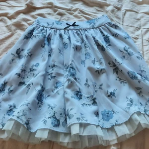 Ank Rouge blå blommig kjol - Säljer en kjol från japanska märket Ank Rouge! Den har en stretchig midja och passar mig som oftast har storlek 36-40! Kan passa mindre och större storlekar. Kjolen är 45cm lång. Inga defekter av vad jag kan se.  Säljer då jag inte gillar rosetten :)