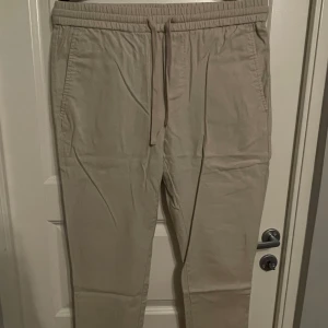 Linne kostymbyxor  - Kostymbyxor i beige färg och linnetyg med resårband i midjan samt snöre upptill. Två fickor framtill samt en fickdetalj baktill.