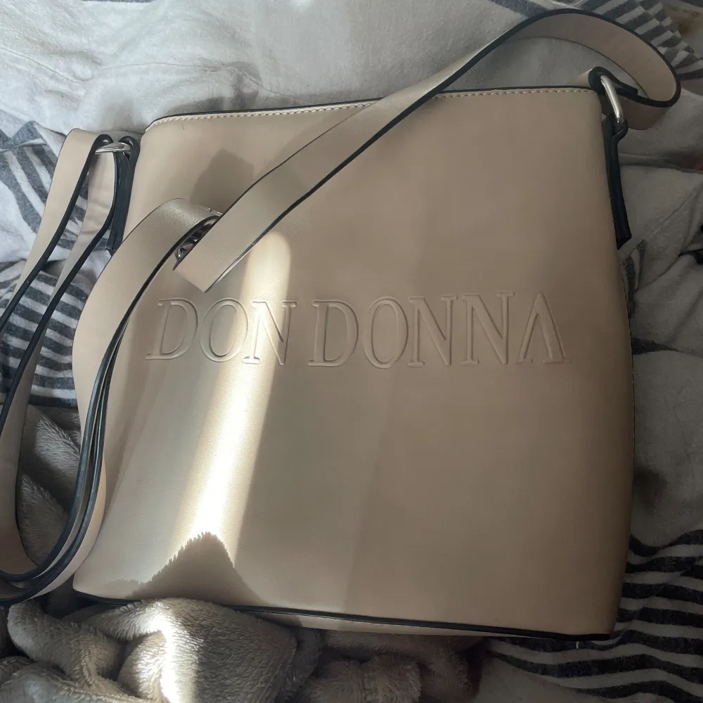 Don Donna väska i fin beige färg, sparsamt använd nästan i nyskick.   Hämtas i Karlshamn/Bromölla eller mot fraktkostnad.. Väskor.