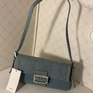 Jeansfärgad handväska - Jeansfärgad handväska från mango med silvrigt spänne. Aldrig använd, prislappen kvar. 