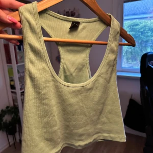 Grön ribbad linnetopp - En grön ribbad topp med breda axelband och rund halsringning. Toppen är ärmlös och har en tight passform. Använt en del men bra skick. Normal i storlek. croppad. 