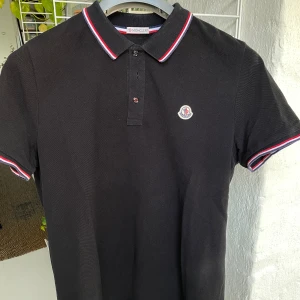 Moncler Pike - Svart piké från Moncler i strl M.  Använd 4-5 gånger.  Avklippt tvätttag men givetvis äkta. Så nära nyskick man kan komma. Nypris: 3600 kr