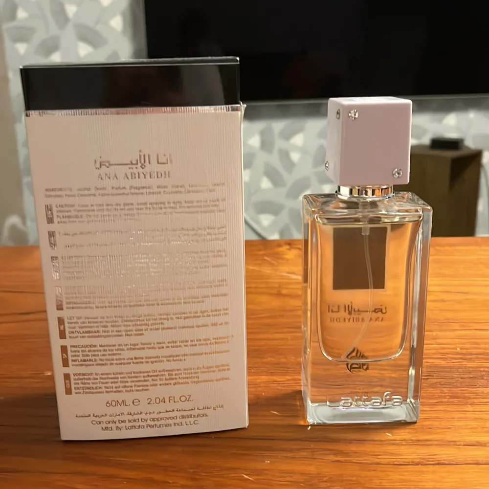 Ana Abiyedh Eau De Parfum från Lattafa är en elegant parfym med en sofistikerad doft. Flaskan är genomskinlig med en vit fyrkantig kork och en guldplatta på framsidan. Förpackningen är vit med guld- och svartdetaljer. Parfymen innehåller noter av trä, mysk och vanilj.. Övrigt.