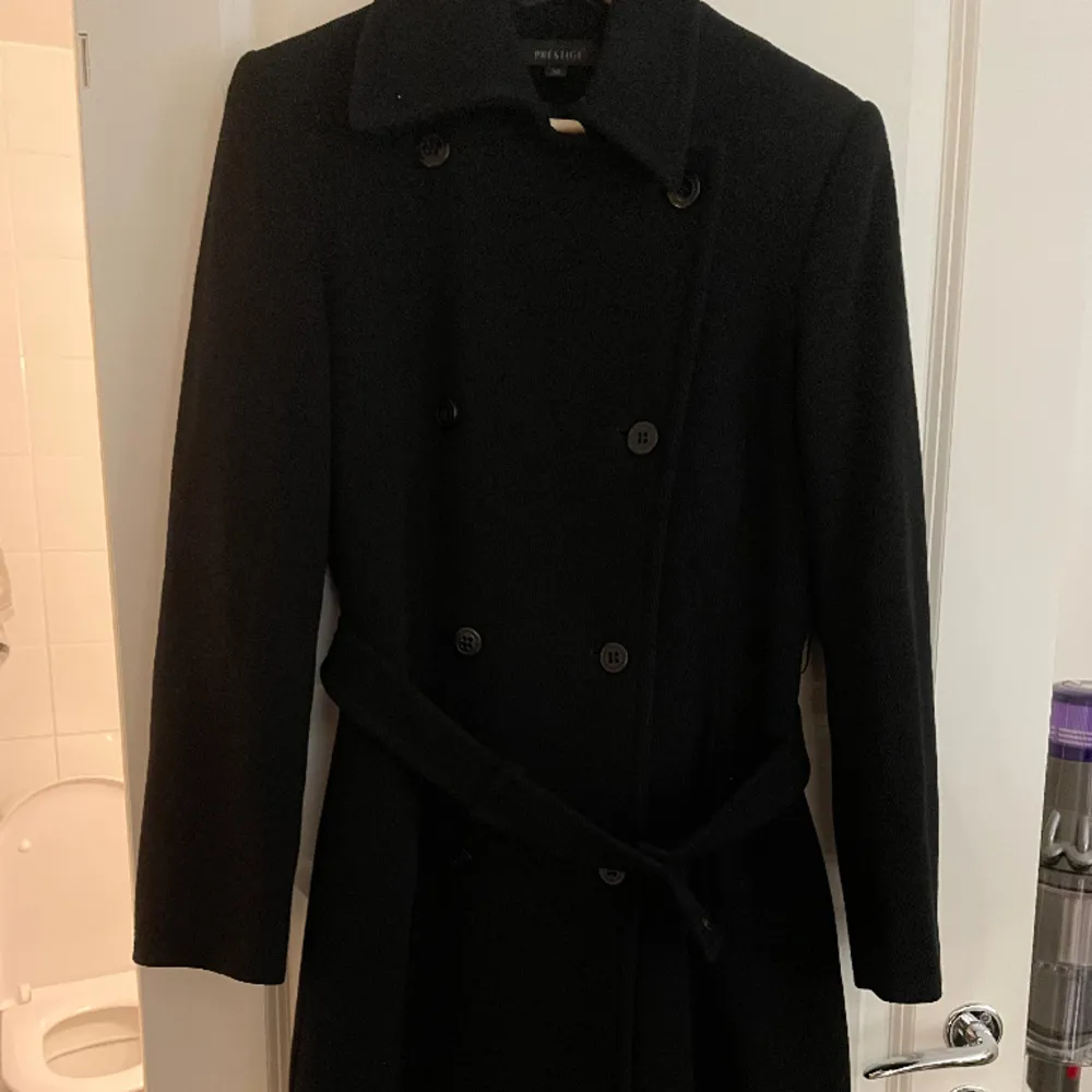 En lång svart kappa köpt på Inwear i storlek 38. Använd fåtal gånger och har märket prestige.. Jackor.