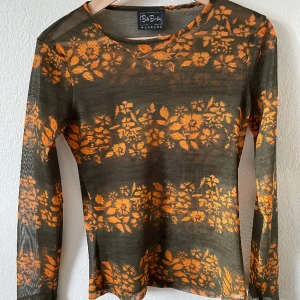 Meshtop  - Fin tröja i mesh. Den är grön och orange med blommigt mönster. Supercool