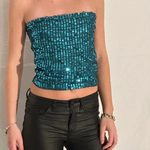 Glittrig bandeautopp  - Glittrig bandeautopp i blågrön/teal. Paljetter på framsidan och ett mjukt stretchigt tyg i ryggen. Tjejen på bilden har i vanliga fall xs