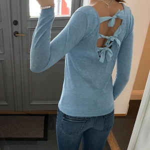 Blå tight tröja med rosetter - Blå tight tröja från Vintage Dressing. Skulle uppskatta att det är storlek S. Band med rosetter i bak. Fint skick. Använd gärna köp nu!