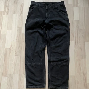 Svarta/ Grå Carhartt double knee - 449kr - Svarta/grå Carhartt double knee jeans i storlek W30xL32. Yttertyg 100% bomull, fickorna 65% polyester & 35% bomull. Dubbel knä, fram & bakfickor, ”carpenter” fickor. Vit textil logga på högra bakfickan. För mått/fler bilder skriv privat.